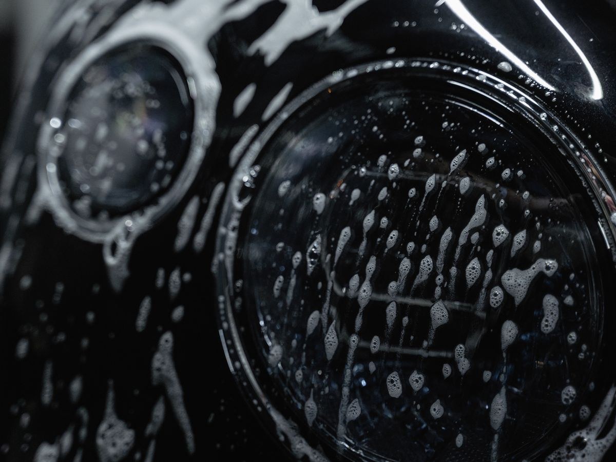 Close-up of soapy foam on glossy headlights during wash